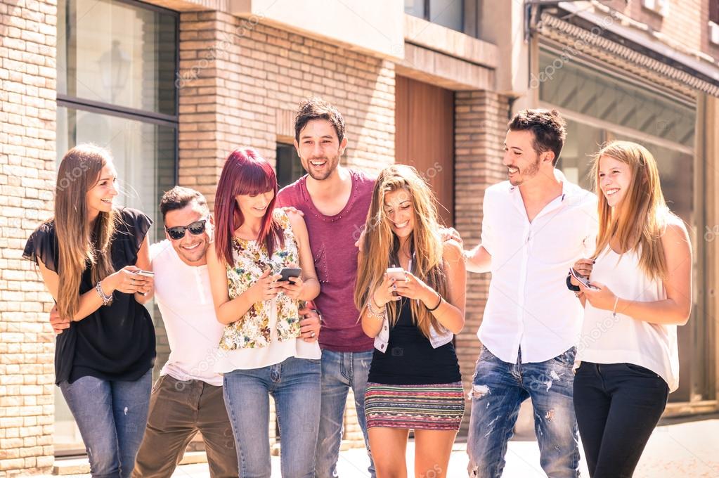 Group of young best friends having fun together walking on town street - Moment of technology interaction in everyday lifestyle - Internet connection spots outdoors - Soft desaturated filtered look