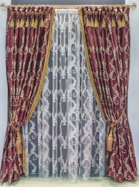 The dense, maroon and the luxurious curtains on the rings are hanging on the metal cornice.