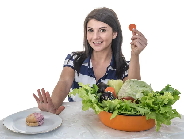 Uma jovem se recusa a comer um queque saboroso e escolhe cenouras e legumes frescos. — Fotografia de Stock