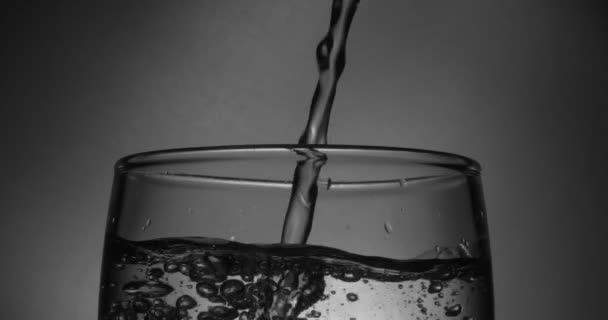 Vatten rinner in i glaset på en svart bakgrund. Super slow-motion. — Stockvideo