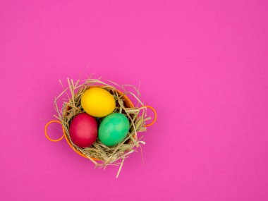 Easter eggs in a bowl on the hay. Bright pink background.