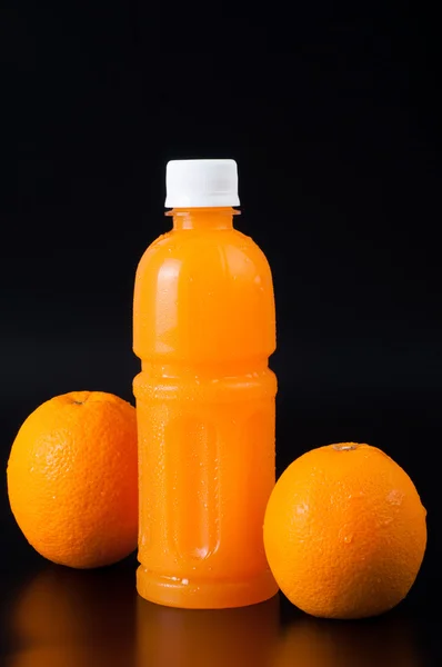 Jus d'orange dans une bouteille et orange à côté isolé sur noir — Photo