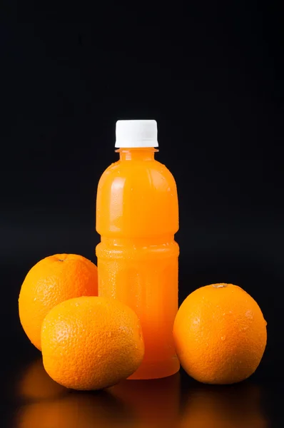 Sinaasappelsap in een fles en oranje ernaast geïsoleerd op zwart — Stockfoto