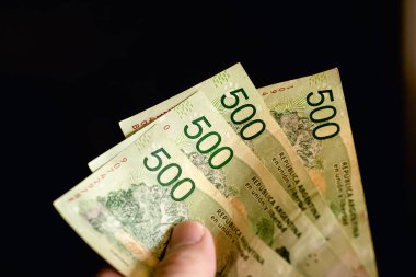 A person holding a group of banknotes of Argentine pesos, the money of the Argentine. Dark background. Photo for representation of economy and finance 