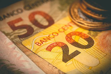 Macro shot of Brazilian Real banknotes with coins on background 