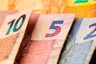 Macro shot of Brazilian Real banknotes with coins on background 