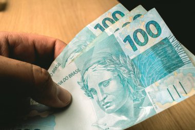 Money, Brazil, Real ( BRL ). A Man holding a Brazilian Real banknotes. 100 real bills.