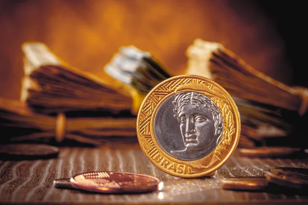 Brazilian money coin real on a wooden object with many banknotes in the golden background.