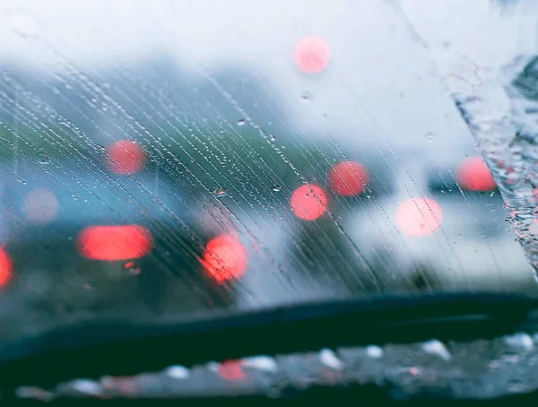 Cars with defocused lights in the rain seen through the front window of an automobile. Glass full of rain drops