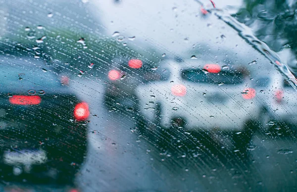 Cars with defocused lights in the rain seen through the front window of an automobile. Glass full of rain drops