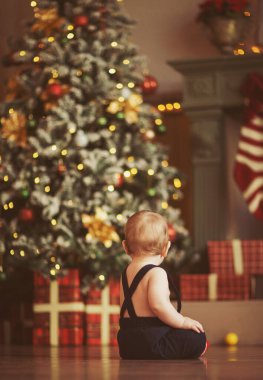 Noel ve Yeni Yıl konsepti. Küçük bebek kameraya arkasını döndü ve hediyeler ve oyuncaklarla güzel bir Noel ağacına baktı..