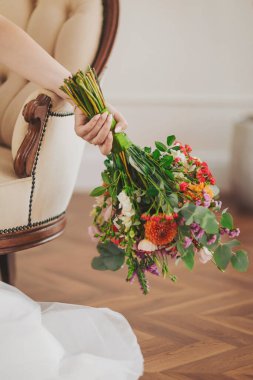 Beautiful bouquet of colorful flowers held by a bride in an elegant room with wooden floors and classic furniture