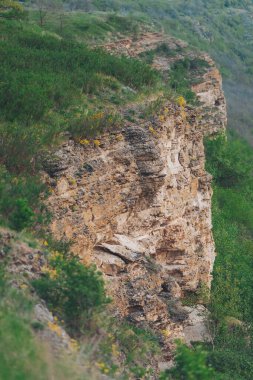 Stunning rocky cliff adorned with green plants during a serene afternoon in a picturesque valley