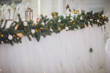 Şenlikli dekorasyonlar, ışıldayan ışıklar, yumuşak örtüler ve bir kış kutlaması için bayram neşesiyle şık bir ziyafet düzenliyor.