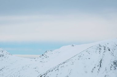 Karla kaplı görkemli zirveler sakin bir kış manzarasında kasvetli bir gökyüzünün altında yükseliyor. Doğanın güzelliğinde keşif ve maceraya davetiye çıkarıyor.