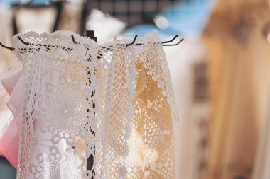 Zarif dantel askılar, parlak öğleden sonra güneşi altında hareketli bir pazar yerinde karmaşık el yapımı altlıkları ve el sanatlarını sergiler.