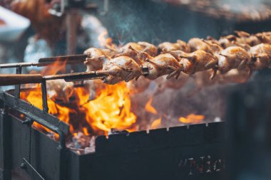 Yazın ortasında canlı bir sokak pazarında, açık alevlerin üzerinde salamura edilmiş tavuk ızgarası.