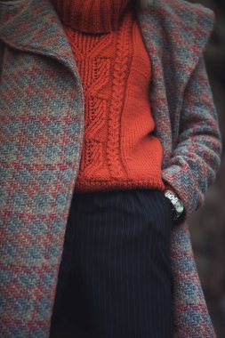 Rahat turuncu bir süveter, desenli bir ceket ve serin sezonda kentsel bir ortamda giyilen şık çizgili pantolona sahip şık bir kış kıyafeti.