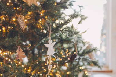 Noel ağacında asılı dekoratif melek süsü sıcak bir şöminenin yanında parlayan ışıklar tatil sezonunda rahat bir atmosfer yaratıyor.