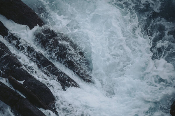 Waves crashing against rocky shoreline at a coastal area during overcast day with gentle ripples and foam creating a serene and natural atmosphere