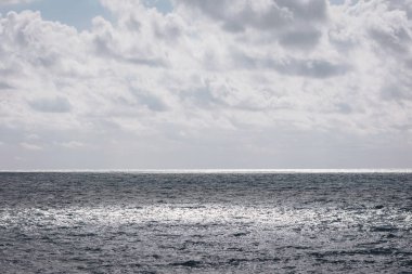 Sakin okyanus dalgaları, kumsalda huzurlu bir günde bulutlu bir gökyüzünün altındaki güneş ışığını yansıtır. Huzurlu bir atmosfer yaratır ve rahatlatıcı bir ortam yaratır.