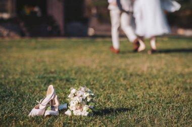 Çiftler çimenlerde yürürken düğün ayakkabıları ve buketler açık hava kutlamalarında dinleniyor.