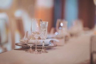 Akşam yemeği için çeşitli cam parçalarıyla dolu bir masayı dekore edilmiş bir yere yerleştirmek.