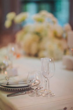 Akşam yemeği için çeşitli cam parçalarıyla dolu bir masayı dekore edilmiş bir yere yerleştirmek.