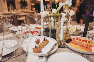 Konuklar et, deniz ürünleri, ekmekler ve içecekler de dahil olmak üzere çeşitli yemeklerle dolu bir masada akşam yemeği yemekten hoşlanıyorlar.