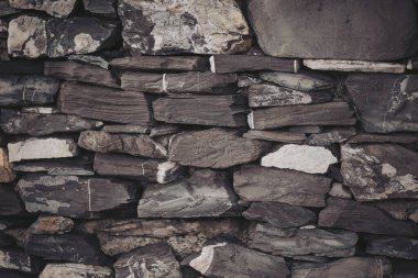 Bir duvar oluşturmak için çeşitli boyut ve renklerde taşlar düzgünce serilmiştir. Düzenleme, her taşın farklı dokularını ve şekillerini vurgulayarak pürüzsüz ve pürüzsüz yüzeyleri gösteriyor.