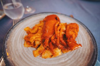 Bir deniz ürünleri tabağı beyaz bir tabağa yerleştirilir. Yemek kalamar ve makarna içeriyor. Yemek masası hazırlanıyor. Yanında çatal bıçak ve bardaklar var.