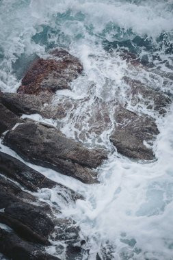 Okyanus dalgaları öğleden sonra boyunca kıyı şeridindeki kayalara çarptı. Sahne, suyun dinamik hareketini katı yüzeylere yansıtıyor, sıçramalar ve sesler yaratıyor.