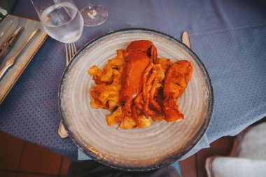 Bir restoranda yanında bir bardak su ve makarna ile bir tabak üzerine bir ıstakoz konur. Dekor, akşam saatlerinde etrafında çarşaf ve çatal bıçak bulunan bir yemek masasını gösteriyor.