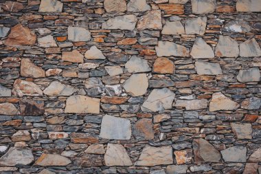 Bir taş duvar farklı şekil ve boyutlarda birbirine yakın sıralanmış taşlar içerir. Duvarda farklı renkler ve dokular var. İnşaatta kullanılan doğal taşları gösteriyor.
