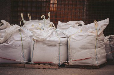 Bir inşaat alanında, paletlerin üzerinde büyük çantaların yanına bir forklift park edilmiştir. İşçiler forklifti malzeme taşımak için kullanabilirler. Ayarlar yoğun ve devam eden inşaat faaliyetlerine odaklanmış durumda.