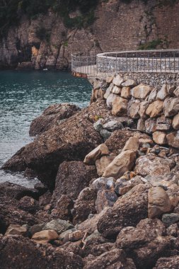 Sahilde bir yürüyüş yolu kıvrılırken kayalar suyun kenarına dizilir. Sahne, kıyı şeridini ve öğleden sonra ışıklarıyla yakındaki kayalıkları yansıtan durgun suyu gösteriyor.