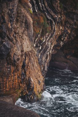 Şafak sökerken dalgalar kıyıya vurur. Zaman tarafından aşınmış uçurumlar, görkemli bir şekilde masmavi denize karşı duruyor, doğanın saf güzelliğini ve sükunetini sergiliyor.