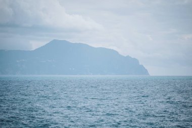 Sakin okyanusta dalgalar dalgalanır. Arka planda görkemli bir dağ yükselir. Bulutlu alacakaranlık gökyüzünün altında sisli ufukla harmanlanır.
