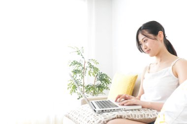 Genç kadın odada dizüstü bilgisayar kullanıyor.