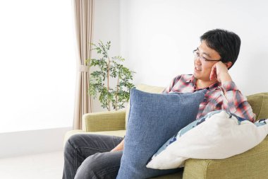 Mutlu Asyalı adam evdeki koltukta oturuyor. 