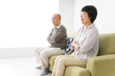 Yaşlı Asyalı çift evdeki kanepede oturuyor.