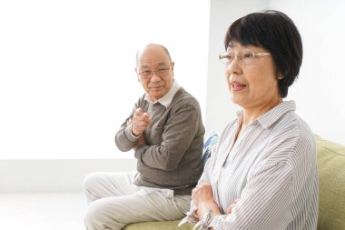 Yaşlı Asyalı çift evdeki kanepede oturuyor.