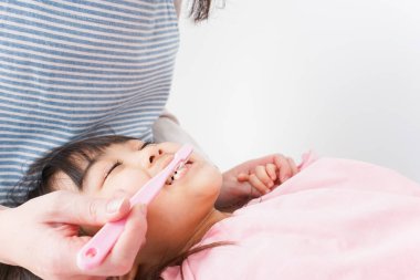 Anne bir çocuğun dişlerini fırçalıyor.