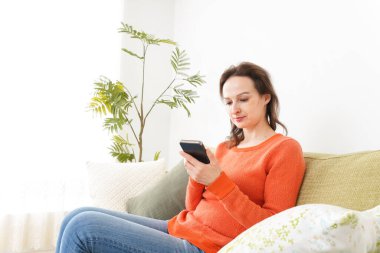 Evde akıllı telefon kullanan genç bir kadın.