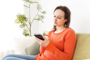 Evde akıllı telefon kullanan genç bir kadın.
