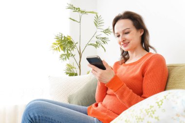 Evde akıllı telefon kullanan genç bir kadın.