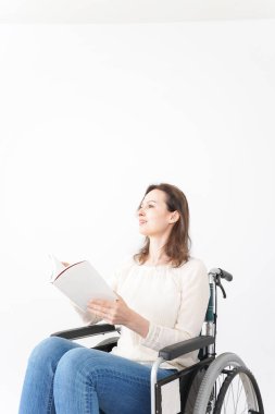 Tekerlekli sandalyede kitap okuyan genç bir kadın.