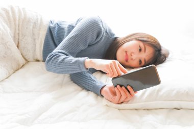 Yatmadan önce akıllı telefon kullanan genç bir kadın. 