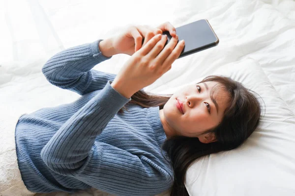 Young woman using smartphone in bed before going to sleep