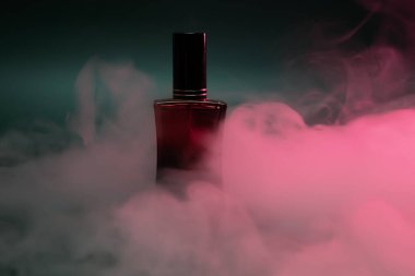 Kırmızı şişedeki parfüm koyu yeşil arka planda buharlı.